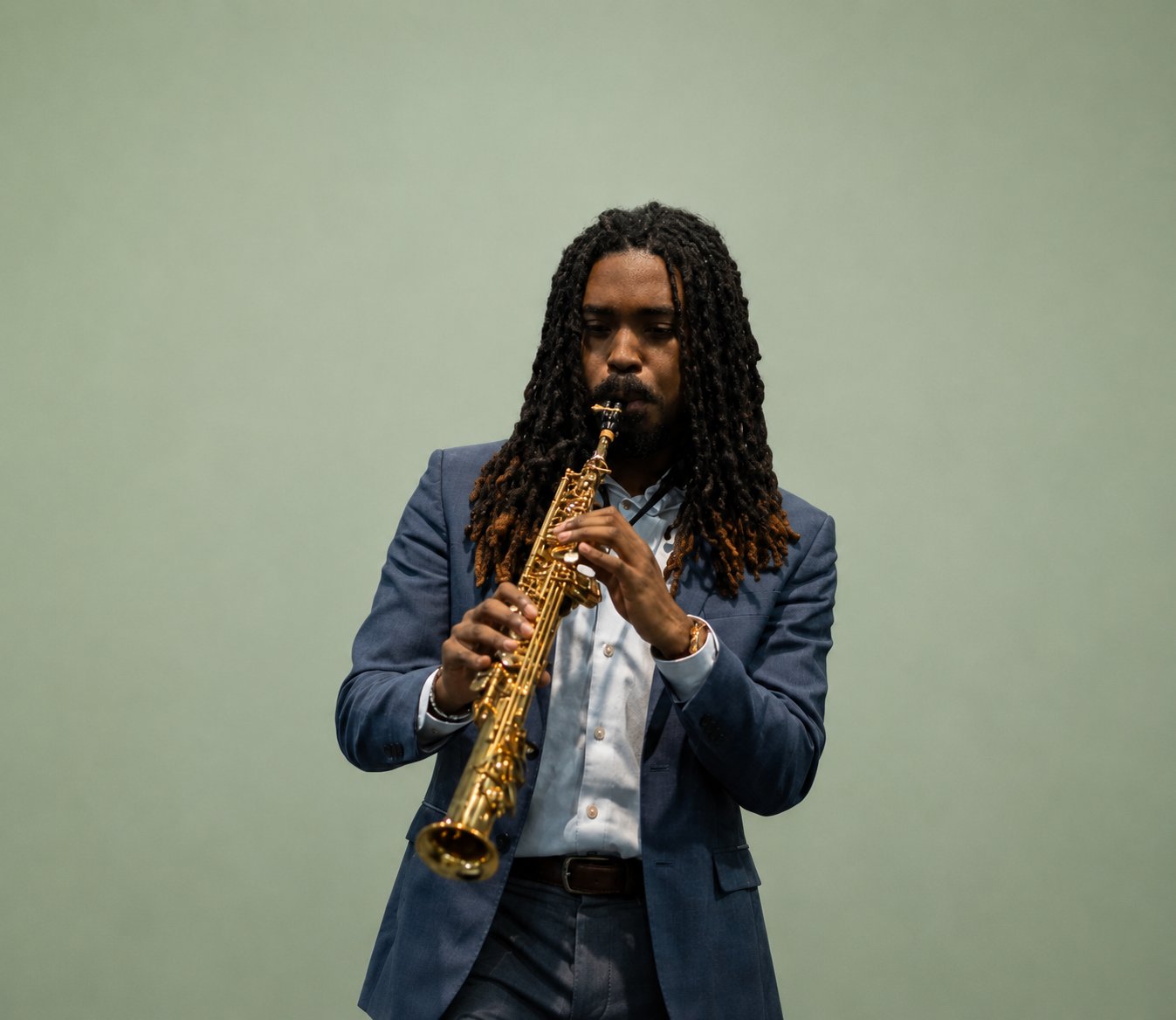 Saxophonist playing soprano sax against a green backdrop